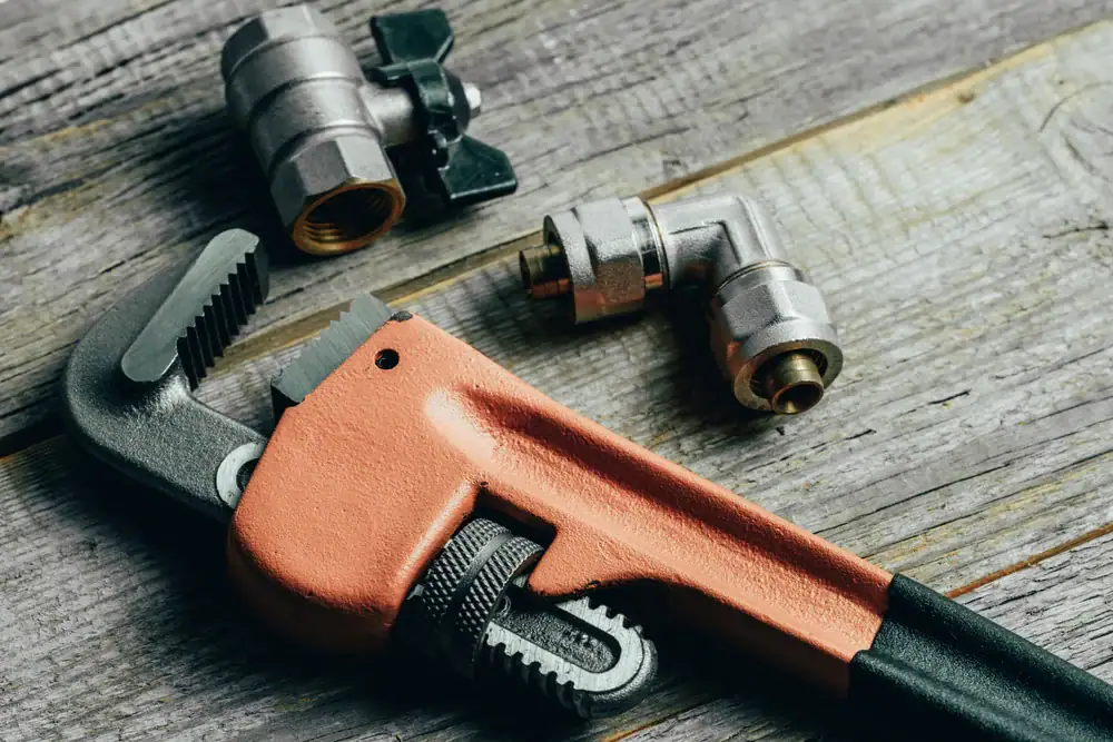 A red pipe wrench and two metal plumbing fittings are placed on a rustic wooden surface, ideal for CA cooling and heating projects in San Jose & Santa Clara County.
